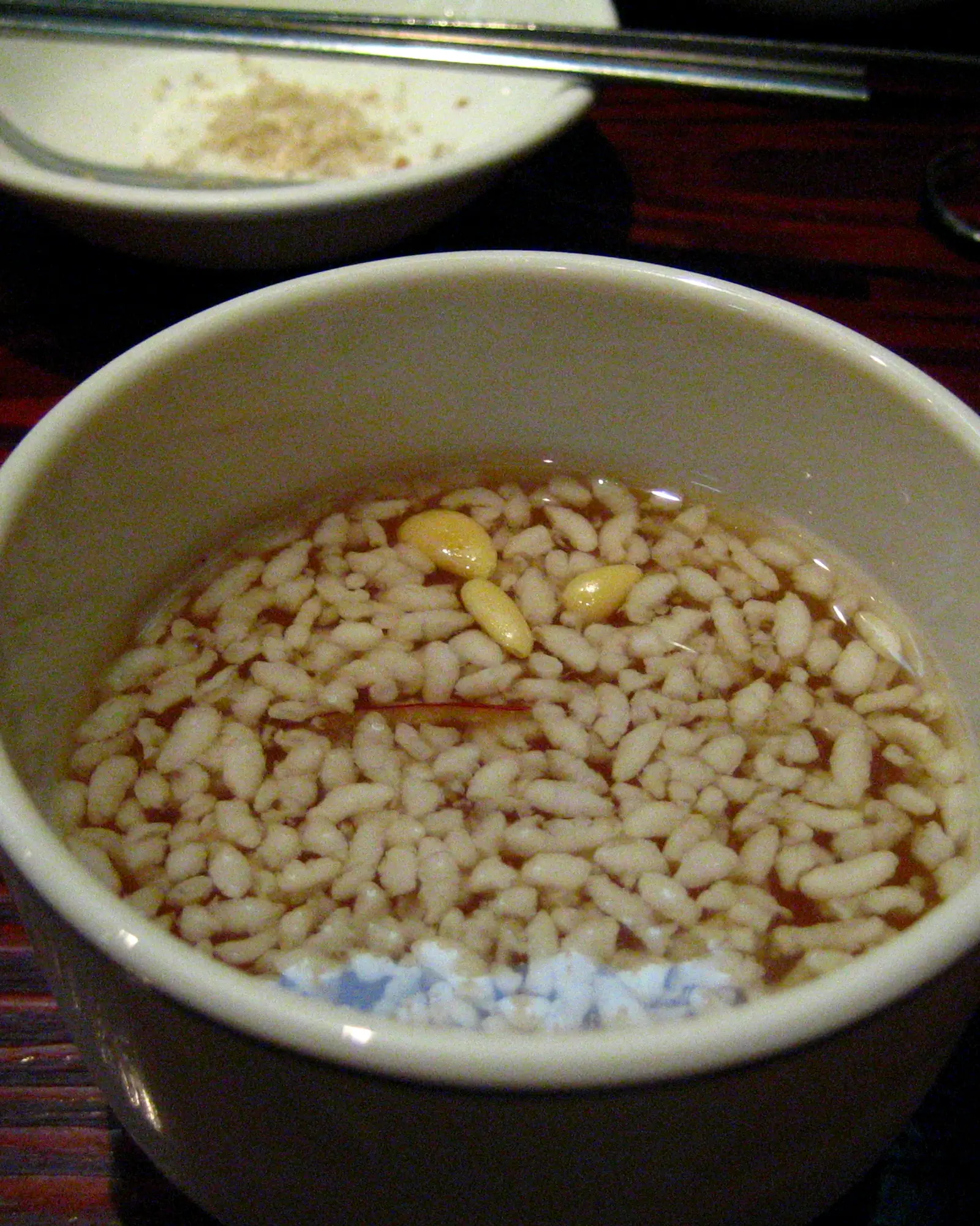 Sikhye (Korean rice punch) in a bowl with cooked rice grains and pine nuts floating on top