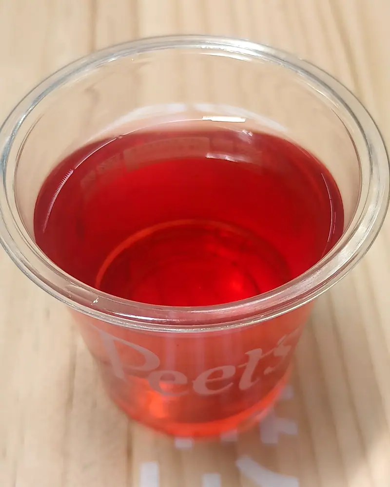 Suanmeitang, a deep red sour plum drink, filled to the brim of a clear plastic cup printed with the Peet's logo