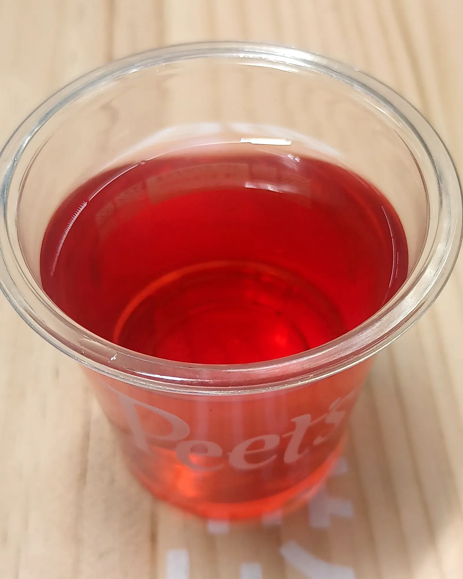 Suanmeitang, a deep red sour plum drink, filled to the brim of a clear plastic cup printed with the Peet's logo