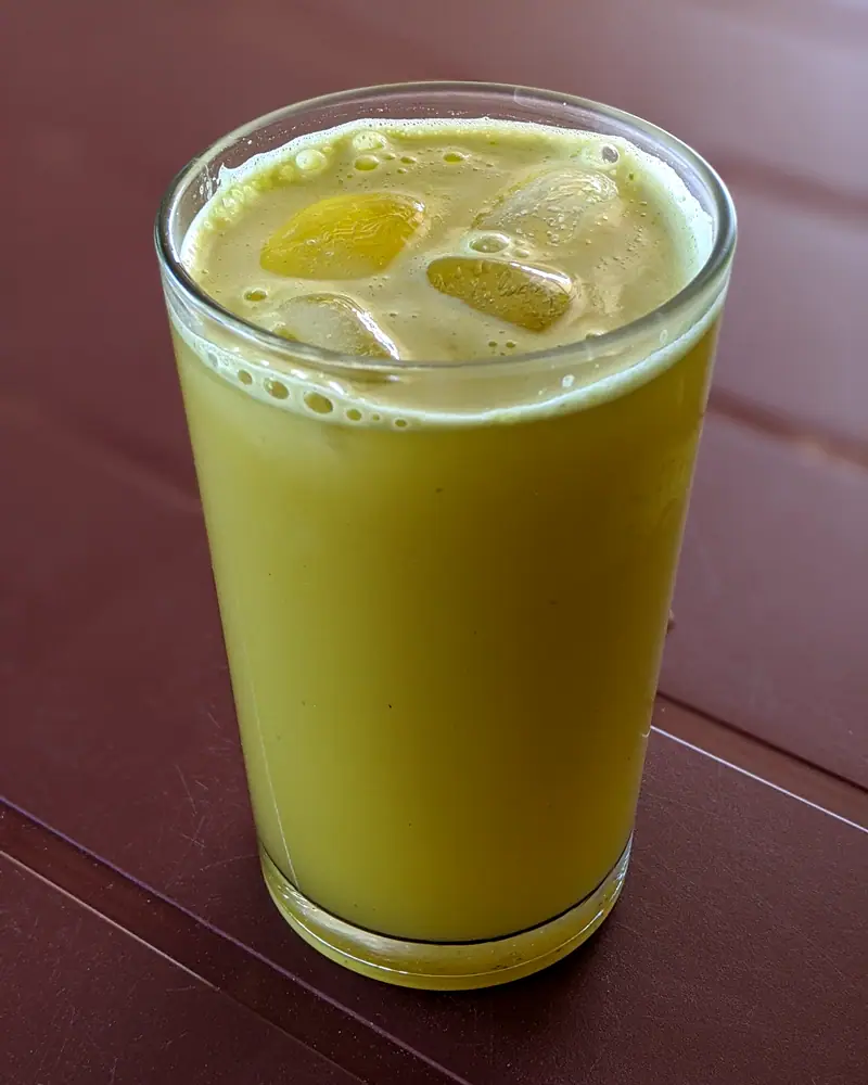 A tall glass of pale green-gold sugarcane juice with lime wedges and ice, photographed from above at an angle