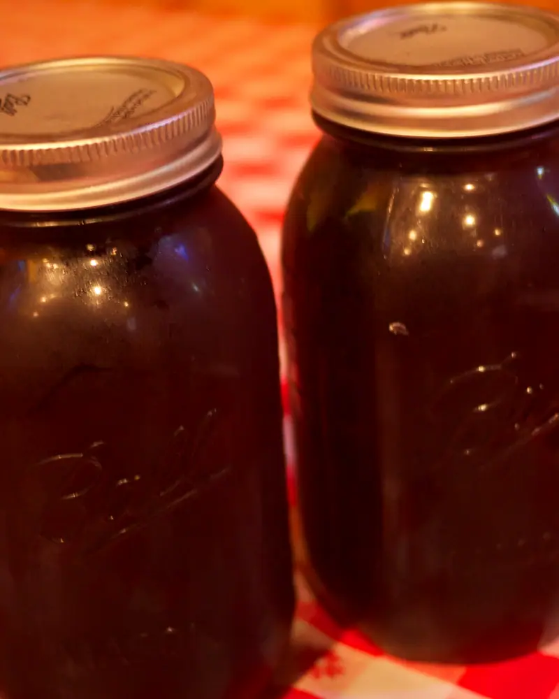 Two mason jars of dark, sweetened iced tea with lids, on a red checked tablecloth