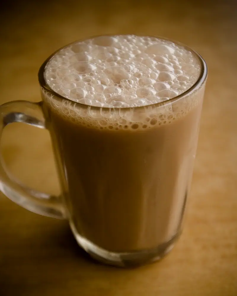 A glass mug of teh tarik, milky tea topped with a thick layer of foam from the pull