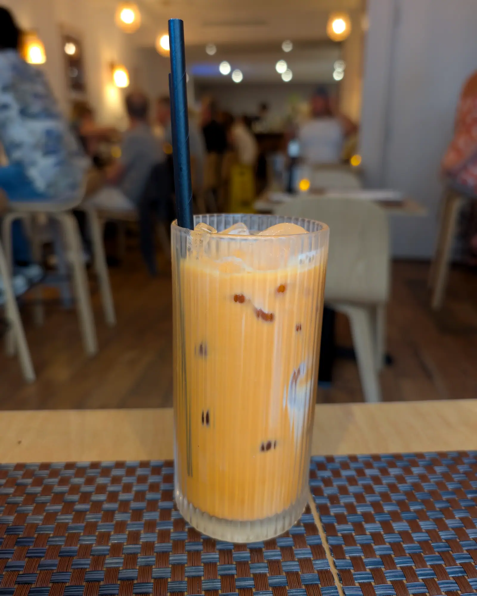 Orange Thai iced tea in a tall glass over ice, with a straw