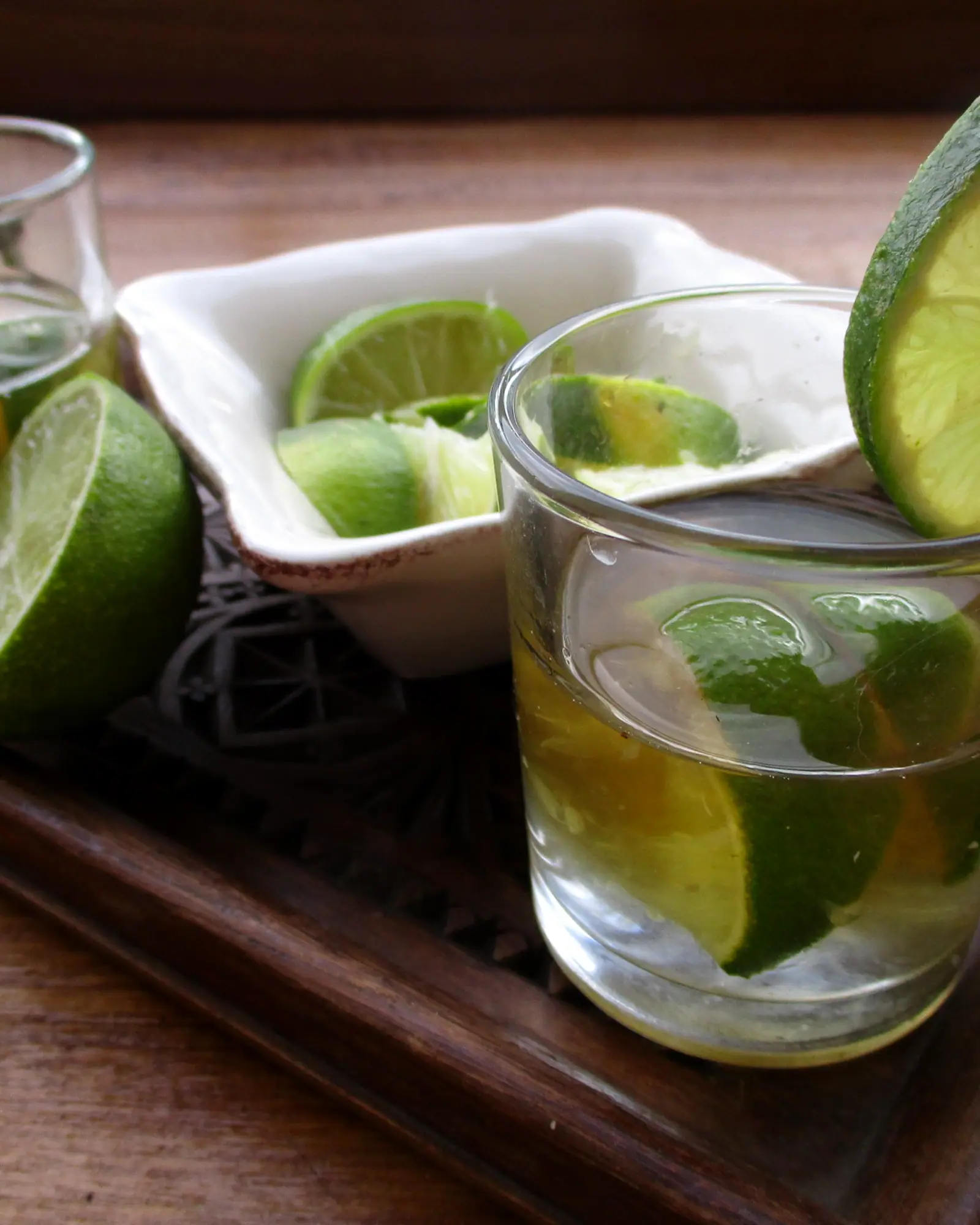 A Ti-Punch in a rocks glass, pale gold rhum agricole with a wedge of lime, surrounded by fresh limes