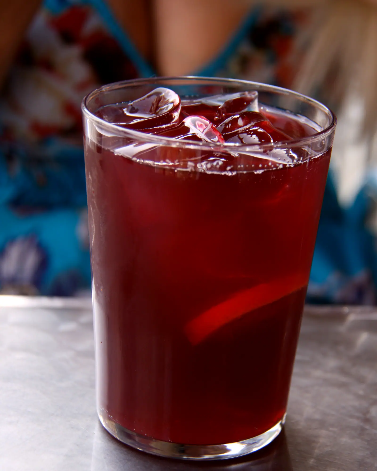 A glass of Tinto de Verano, deep red, over ice with a slice of lemon, on a metal table