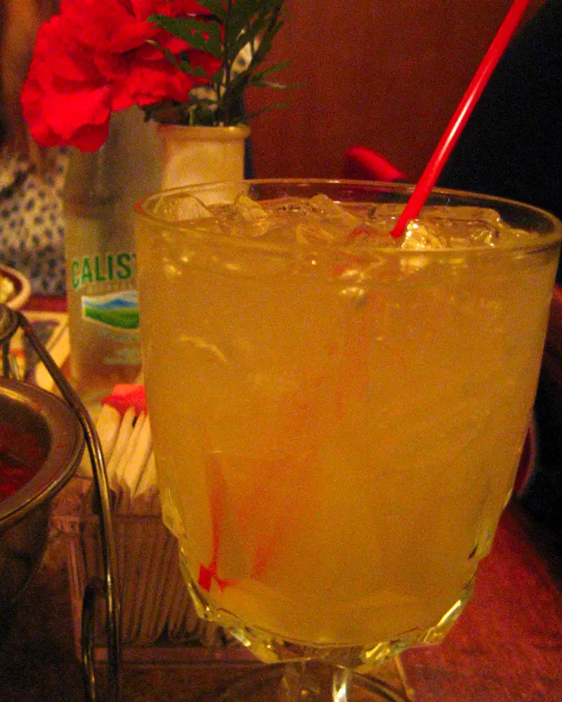 A Tommy's Margarita, pale gold over ice in a rocks glass with a red straw