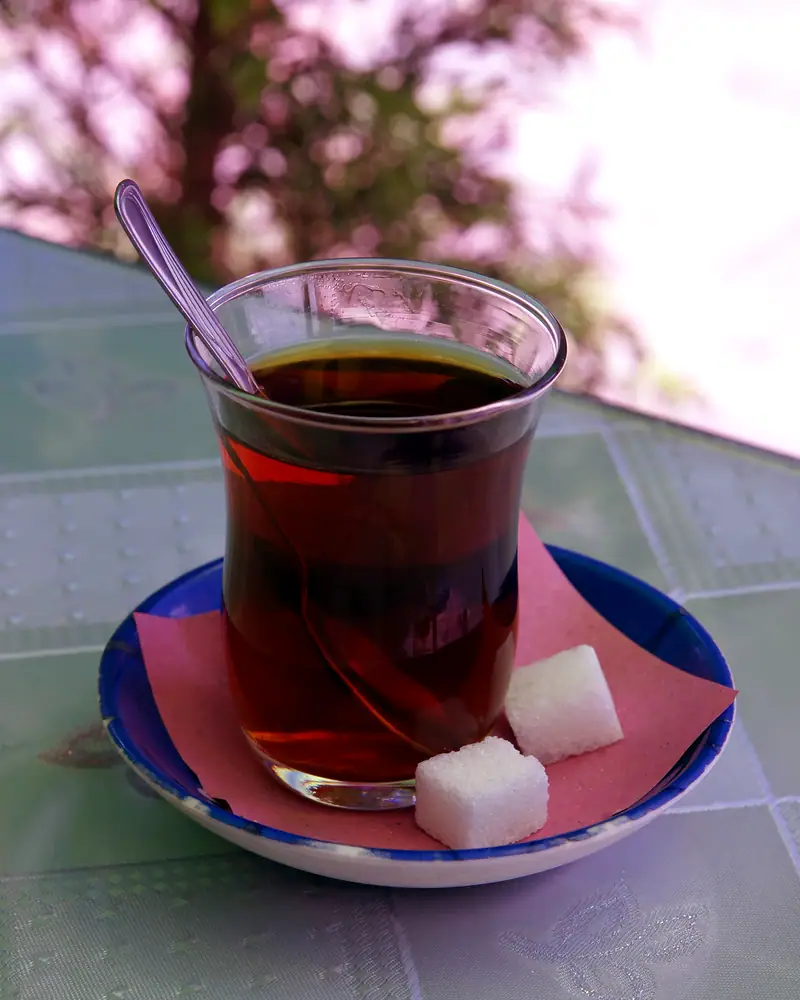 A tulip-shaped glass of Turkish tea on a saucer with sugar cubes and a spoon