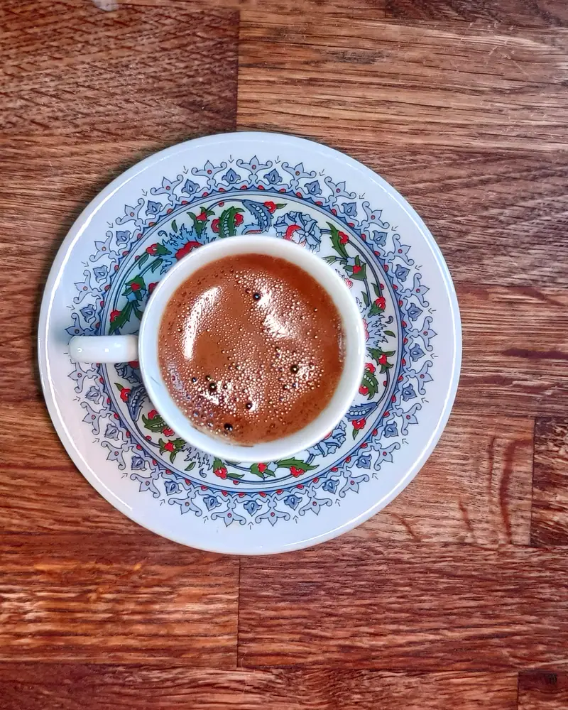 A small cup of Turkish coffee with a thick reddish-brown foam, on a patterned saucer, seen from above