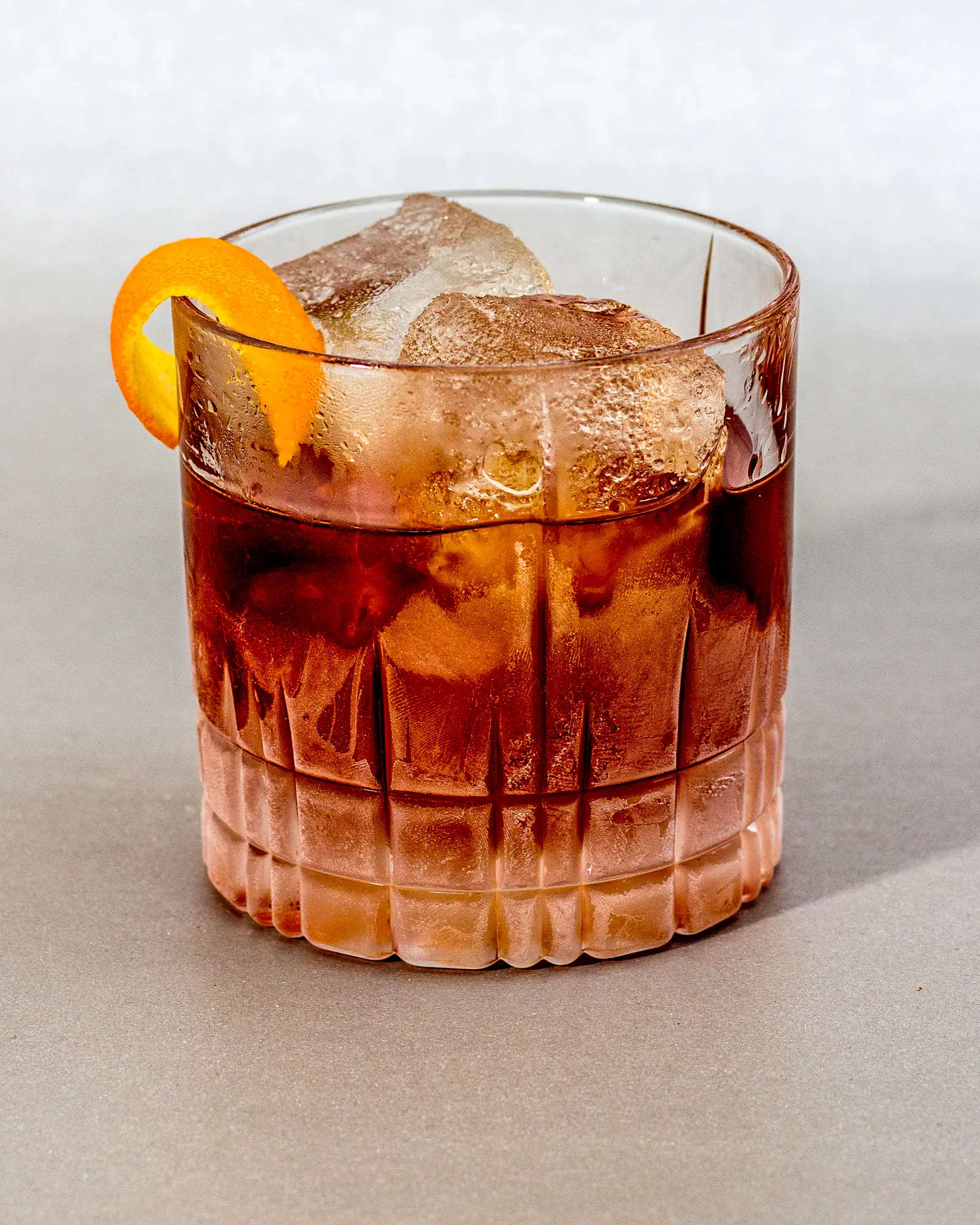 A Vieux Carre served over ice in a rocks glass, deep reddish-amber, with an orange twist against the rim