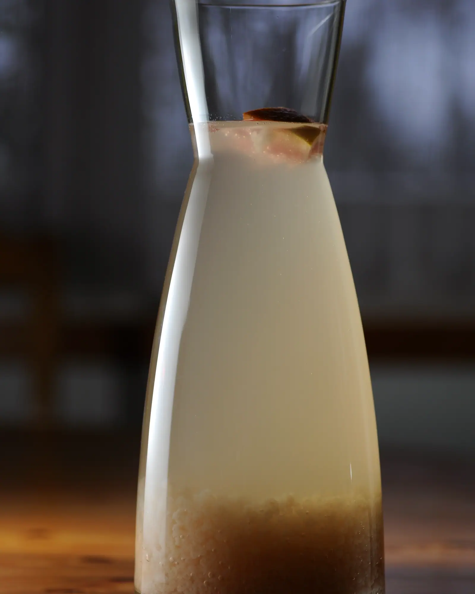 A carafe of pale, faintly cloudy fermented water kefir with a raisin floating near the surface