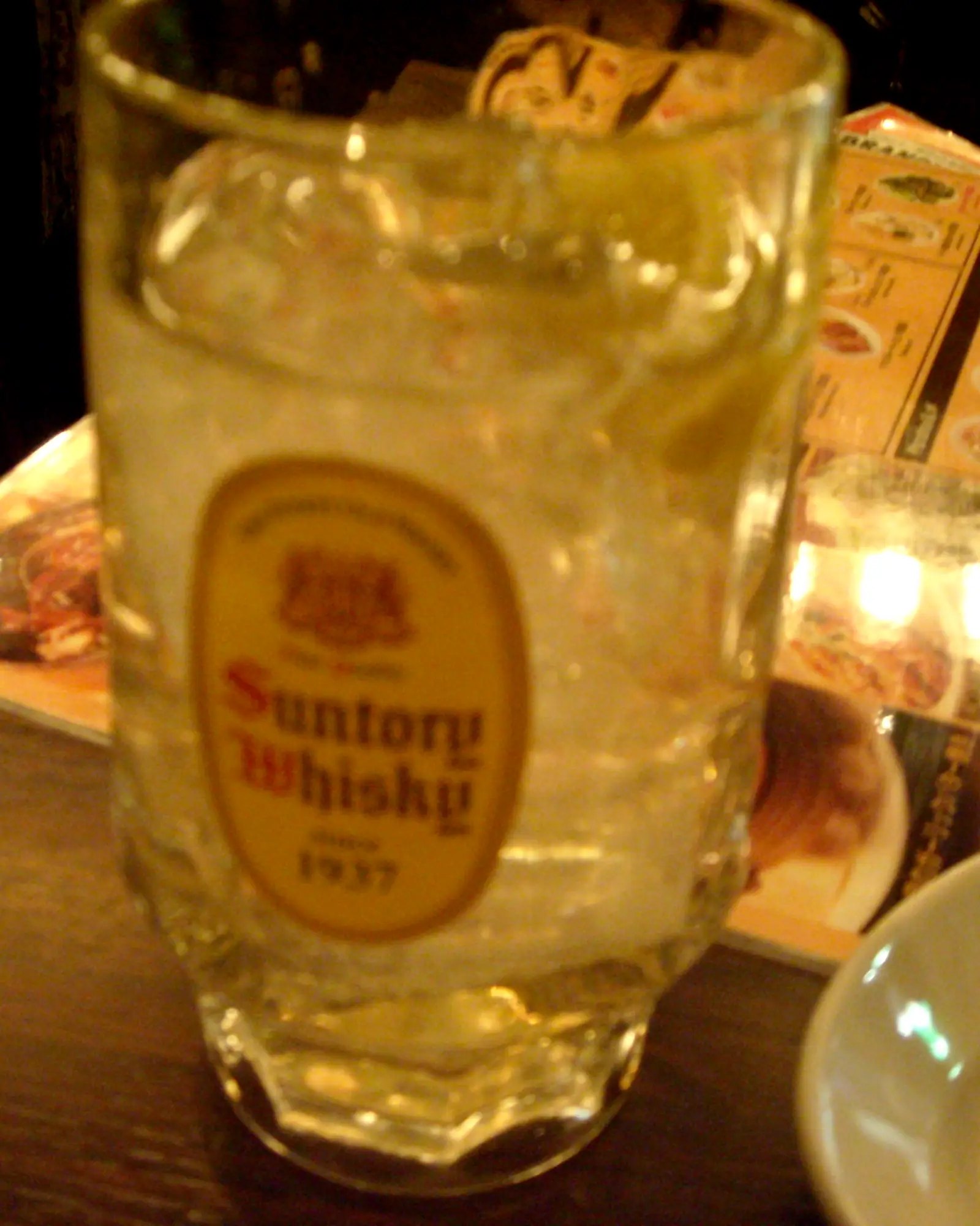 A whisky highball in a tall glass with a Suntory Whisky glass label, pale gold over ice with condensation on the glass