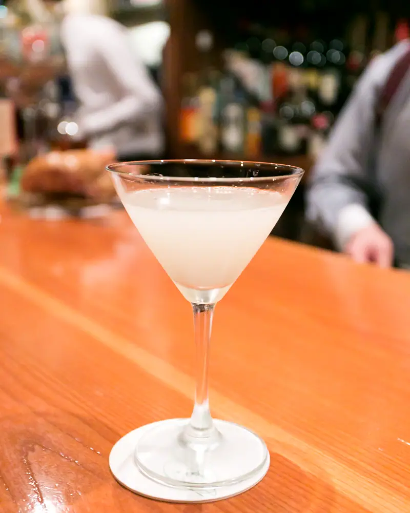 A pale, milky-white White Lady served up in a cocktail glass on a bar counter