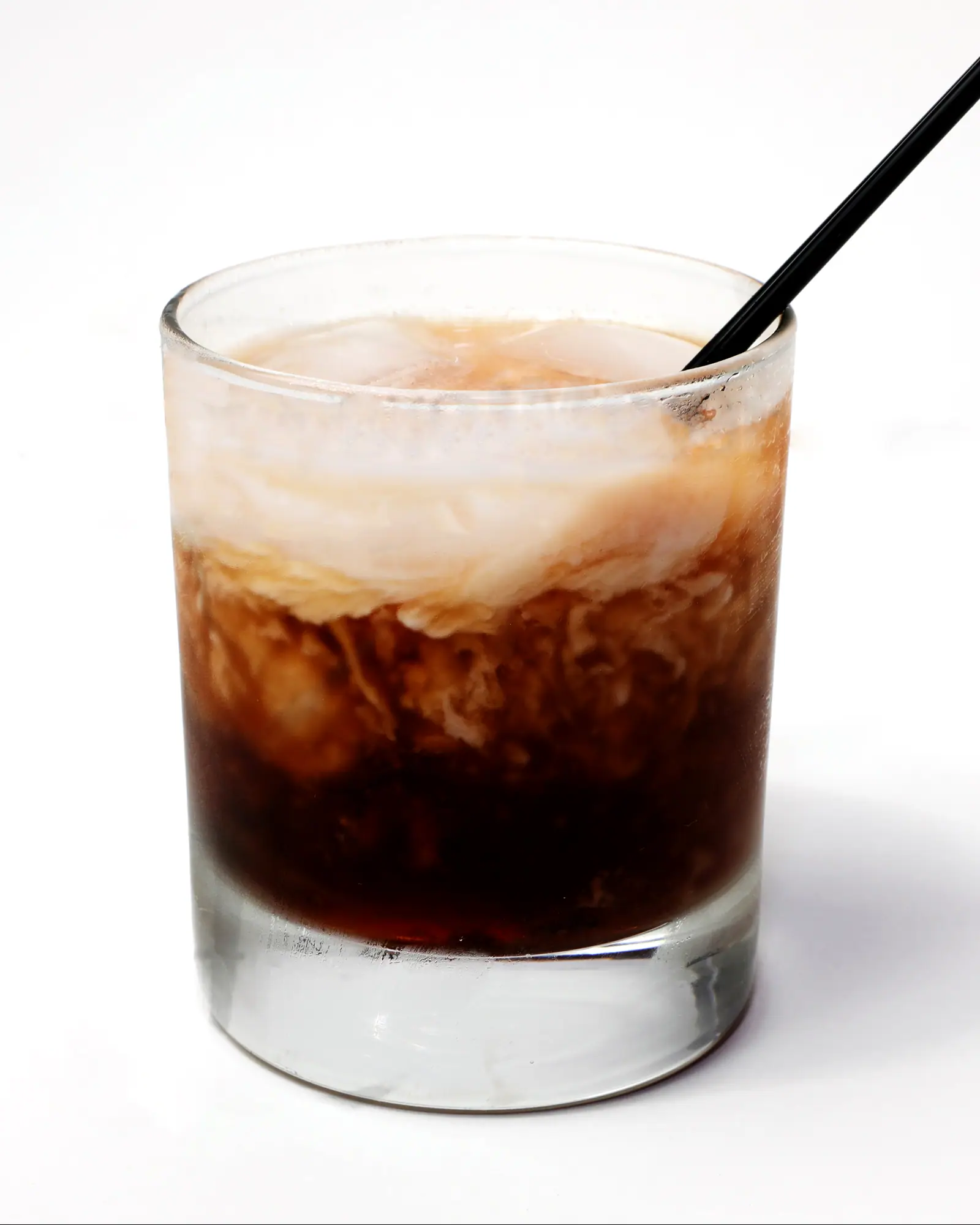 A White Russian in a rocks glass over ice, cream layered pale over the dark vodka and coffee liqueur beneath