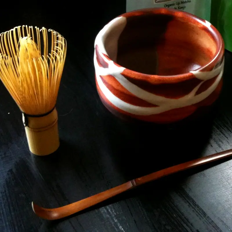 An empty ceramic chawan matcha bowl beside a bamboo whisk and scoop