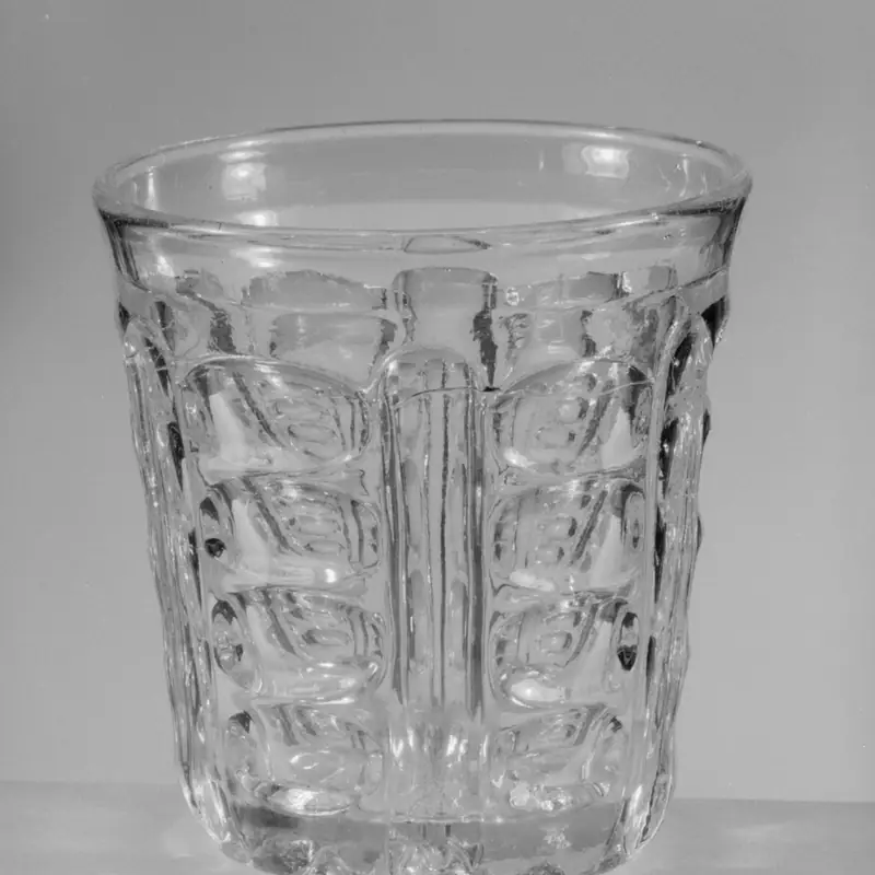 An empty, clear glass tumbler with a diamond-cut pattern, on a plain background