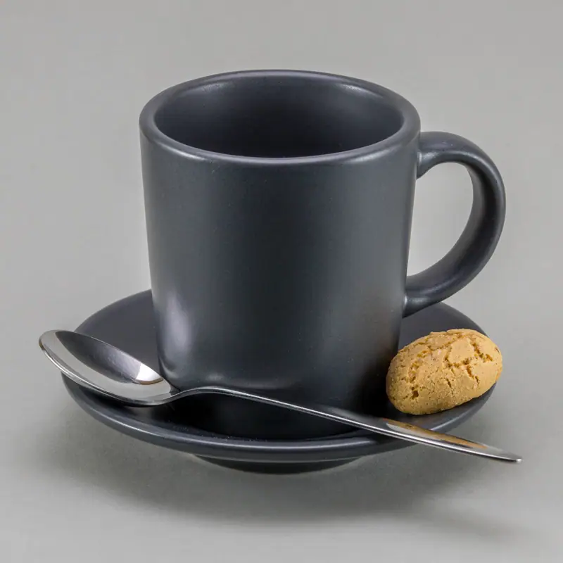 An empty matte gray espresso cup on its saucer, with a spoon and an amaretti biscuit beside it