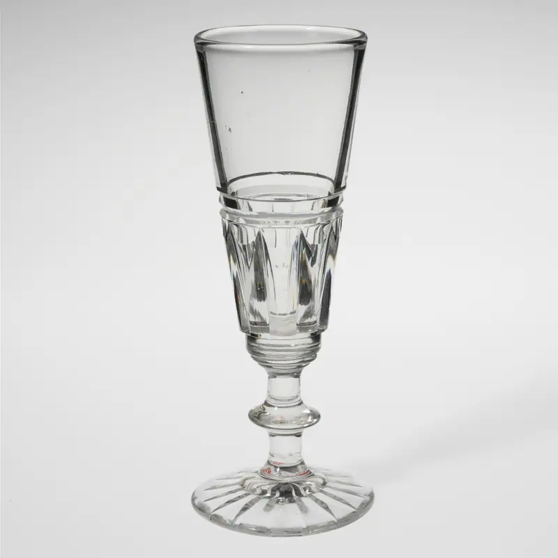 An empty, tall antique champagne flute with a cut-glass stem, on a plain background