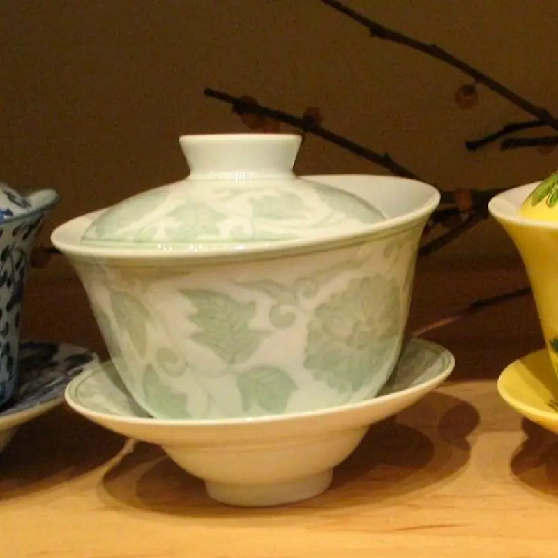 A yellow porcelain gaiwan painted with flowers, its lid in place, sitting on its matching saucer
