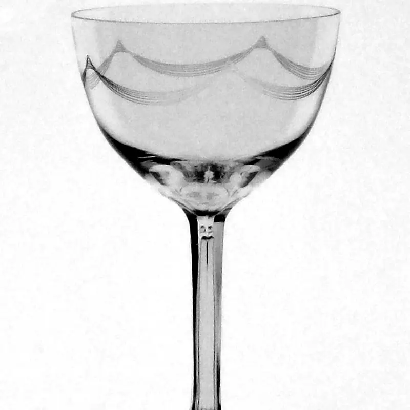 An empty Nick and Nora glass with a wide bowl on a tall thin stem, etched with a decorative pattern