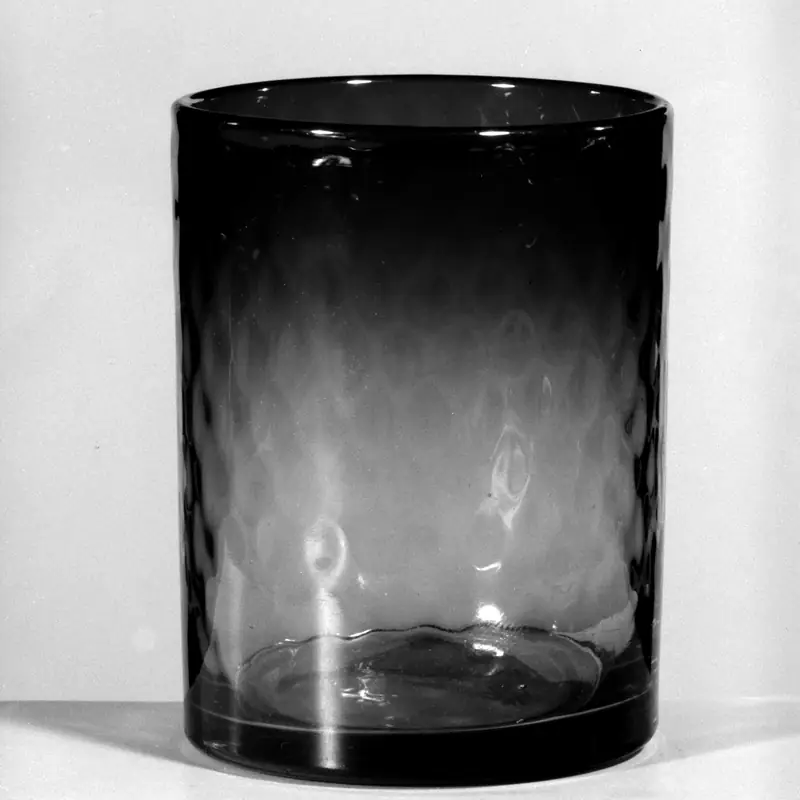 An empty heavy-based tumbler in smoke-grey glass, straight-sided, photographed against a pale ground