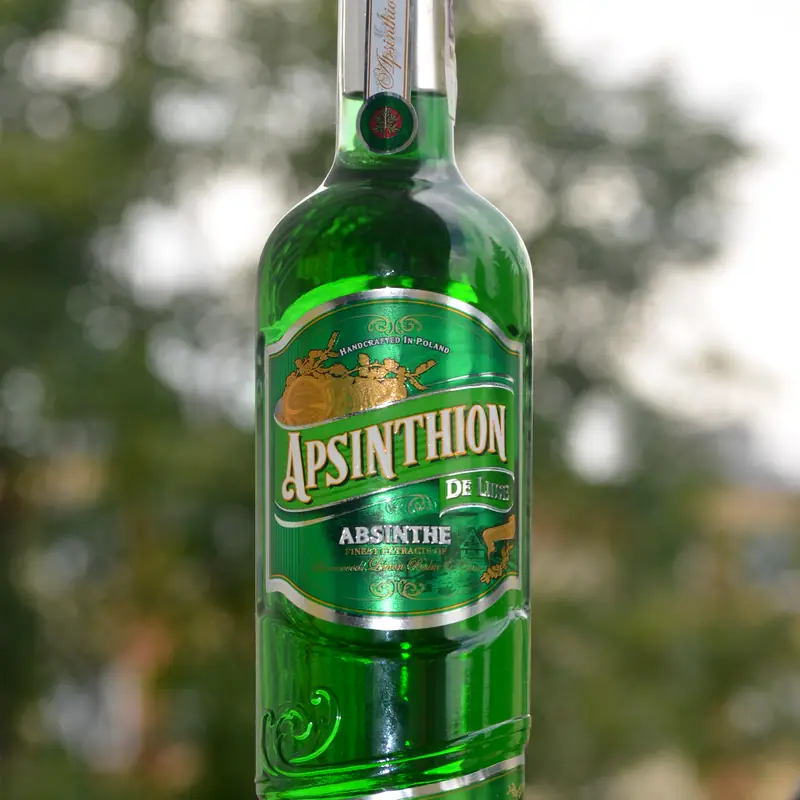 A tall green bottle of absinthe labelled Apsinthion, photographed outdoors against blurred foliage