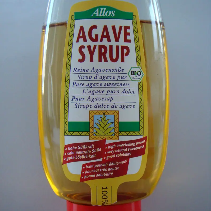 An inverted squeeze bottle of pale gold agave syrup standing on its cap