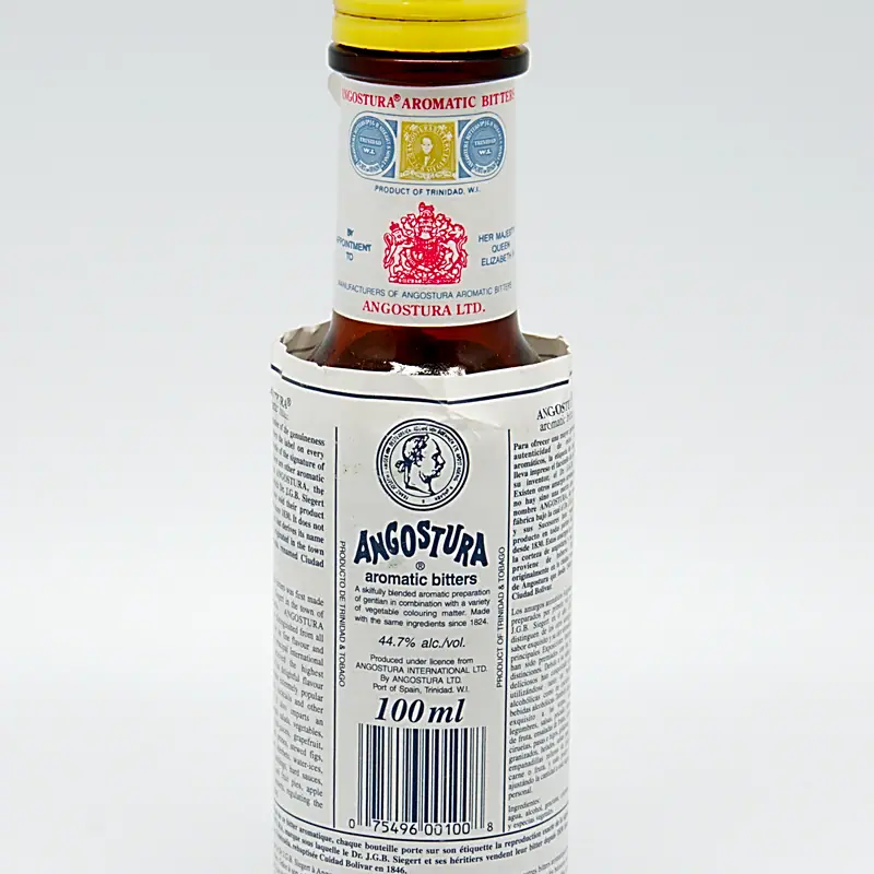A bottle of Angostura aromatic bitters, oversized white label wrapped around dark glass, yellow foil cap, against a plain background.