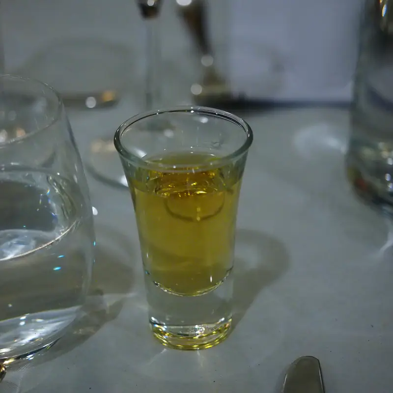 A small shot glass of pale amber-yellow aquavit on a table