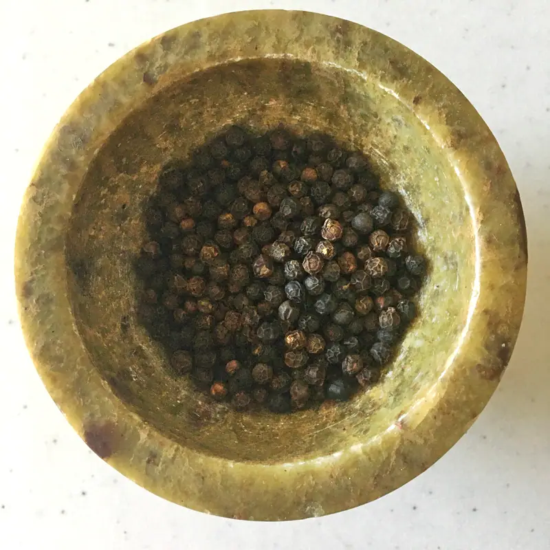Whole black peppercorns filling a small stone mortar