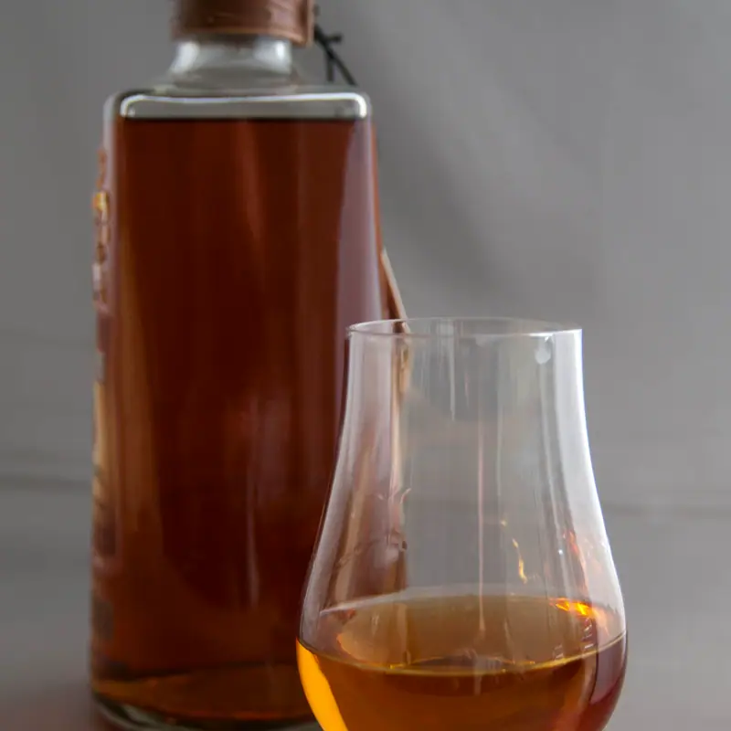 A tulip-shaped nosing glass of amber bourbon standing beside its bottle