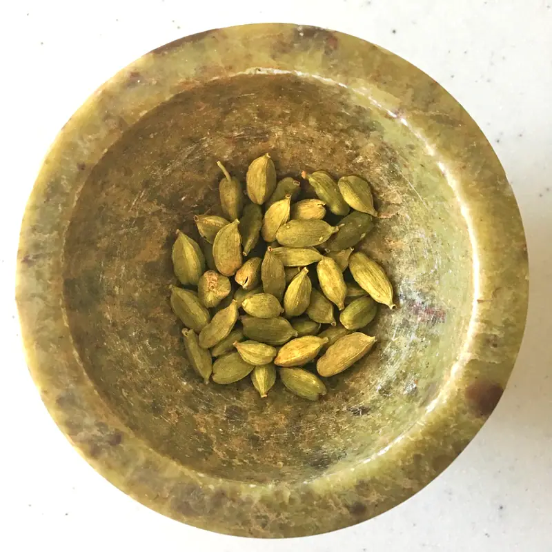 Whole green cardamom pods gathered in a small brass mortar