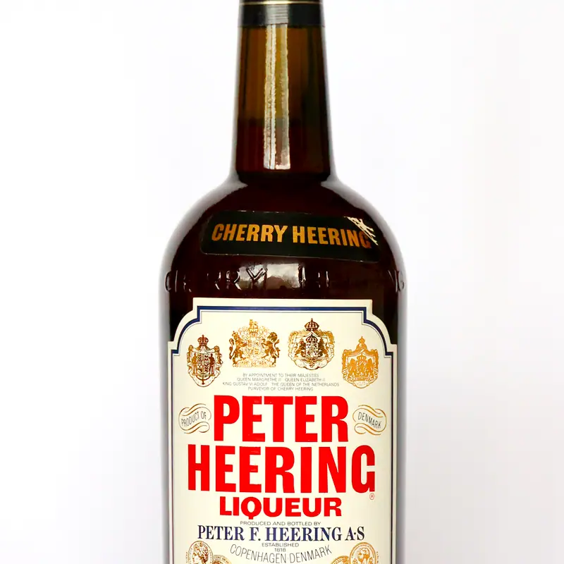 A bottle of Peter Heering cherry liqueur, dark amber glass with a cream label showing a crest and the Cherry Heering name in gold on the neck