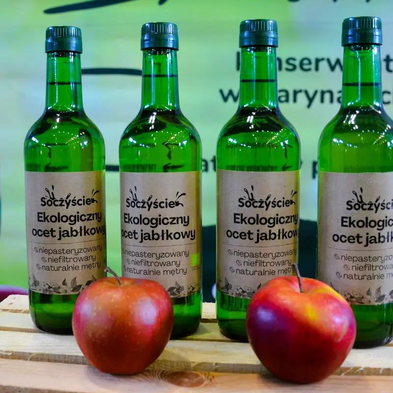 Green glass bottles of unpasteurised apple cider vinegar on a market stall, with apples beside them