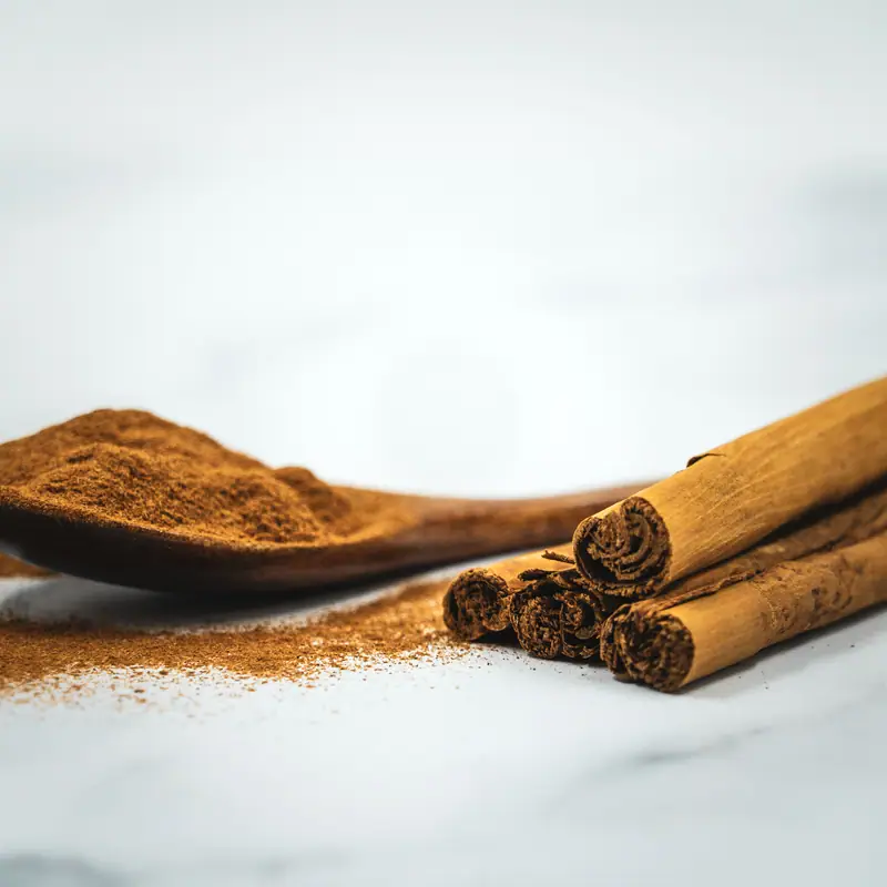 Rolled cinnamon quills on white marble beside a spoon of ground cinnamon