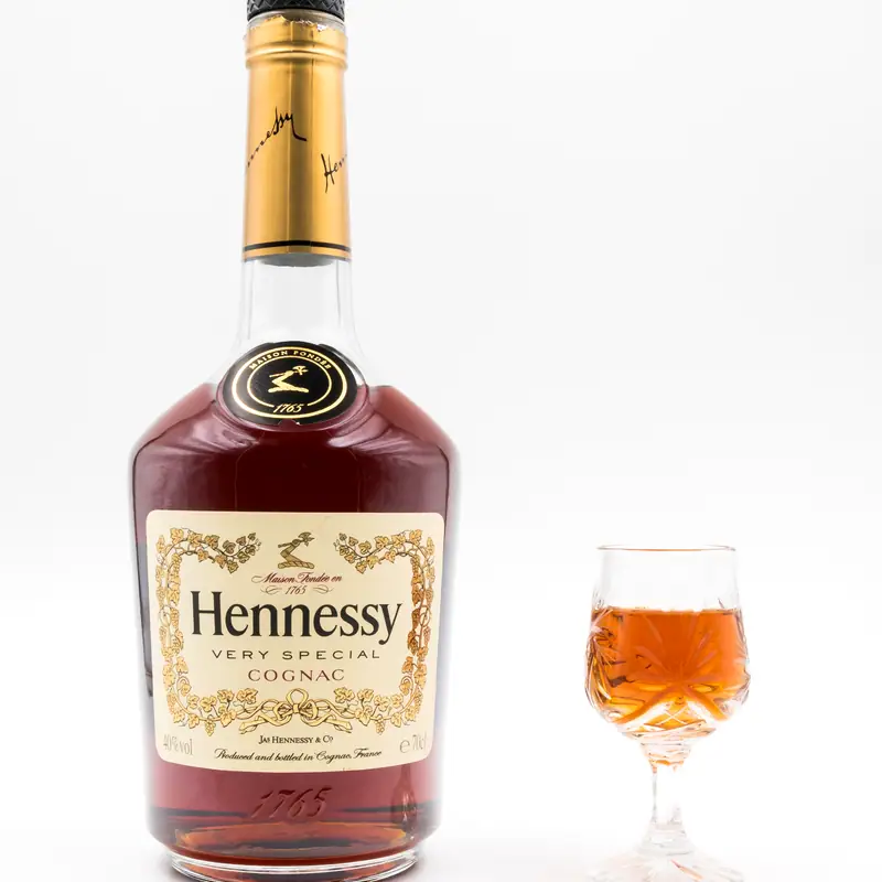 A bottle of Hennessy V.S. Cognac beside a small glass of the amber spirit, against a plain white background