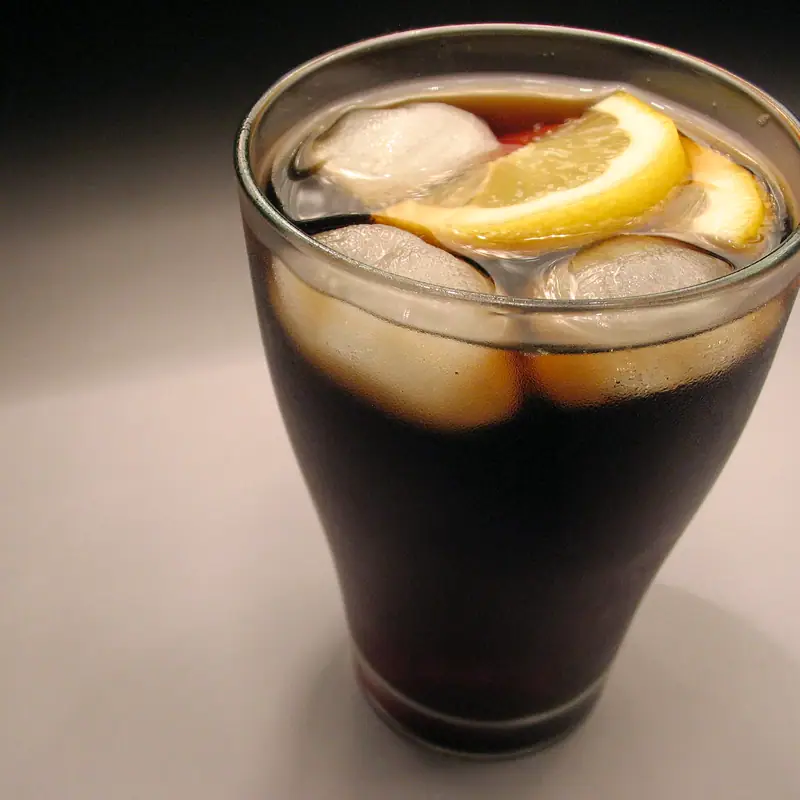A plain glass of dark cola over ice, garnished with a lemon wedge