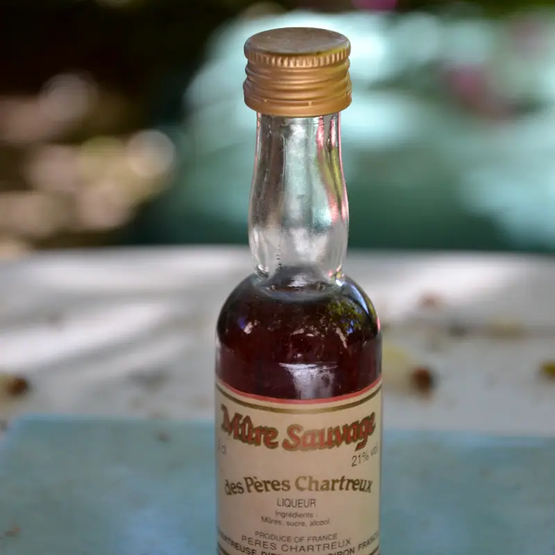 A small bottle of blackberry liqueur lying on its side, showing the dark red-purple liqueur through the glass neck