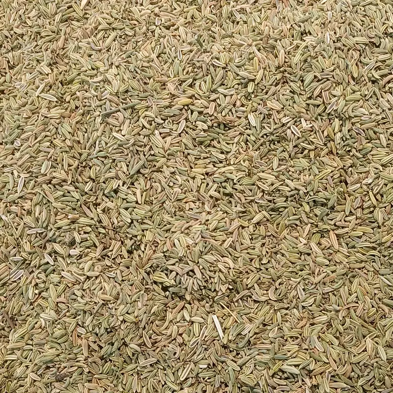 A close-up mass of dried cumin seeds, narrow ridged tan-green seeds