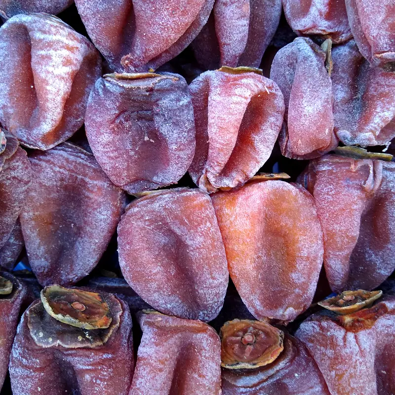 A close pile of dried persimmons with a white sugary bloom on the skin