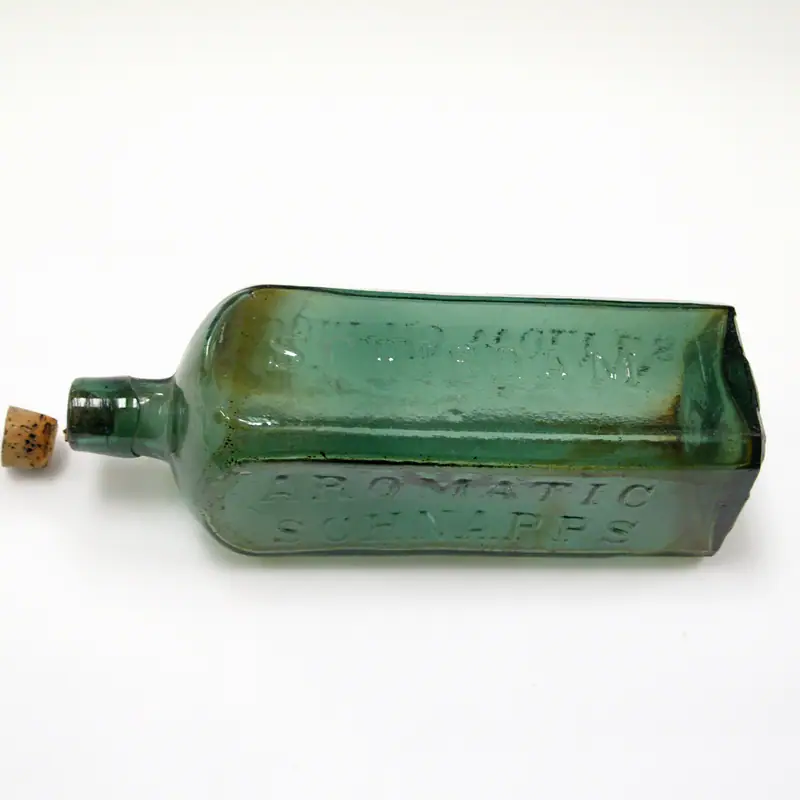 An antique square-shouldered case-gin bottle in green glass, lying on its side with its cork beside it