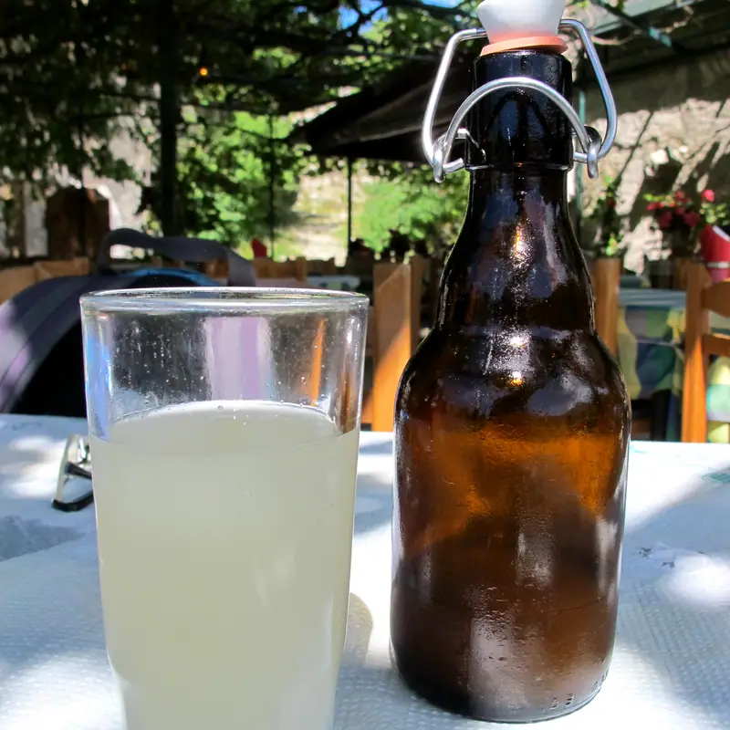 A swing-top bottle of cloudy, pale homemade ginger beer beside a poured glass, outdoors on a table