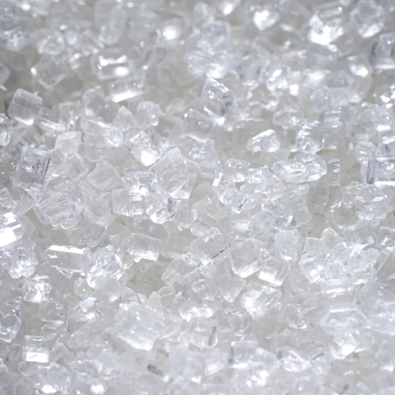 A close view of coarse white sugar crystals lit from the front, each crystal catching the light