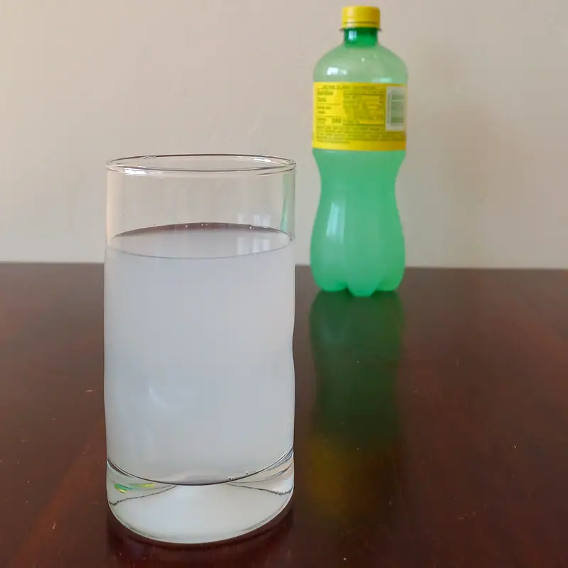 A bottle of Squirt grapefruit soda beside a glass poured with pale soda