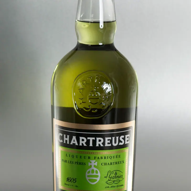 A bottle of green Chartreuse beside a small glass of the liqueur