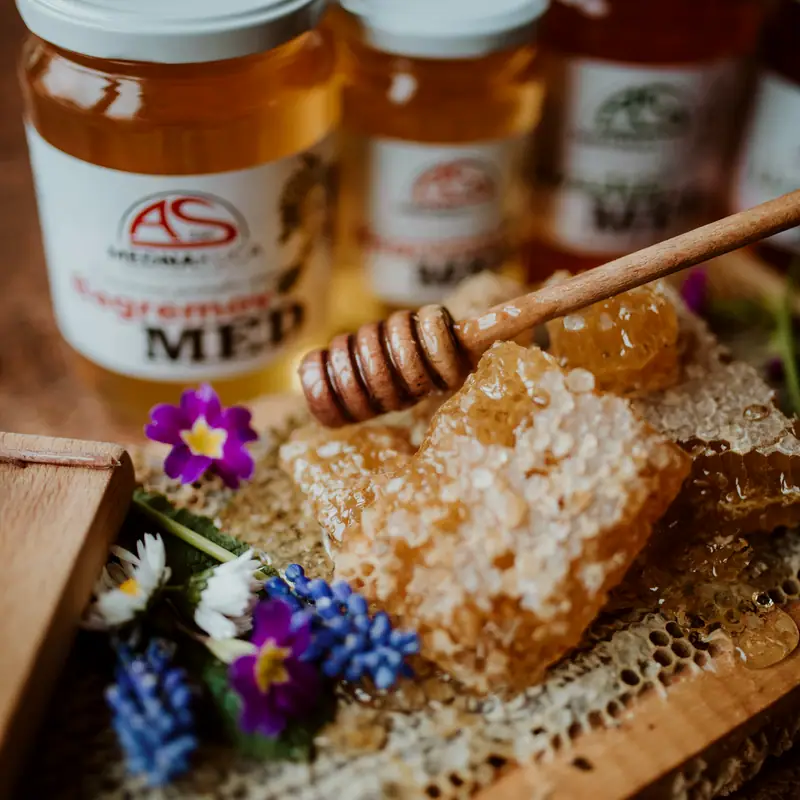 A wooden honey dipper resting on cut honeycomb beside open jars of honey, with spring flowers alongside