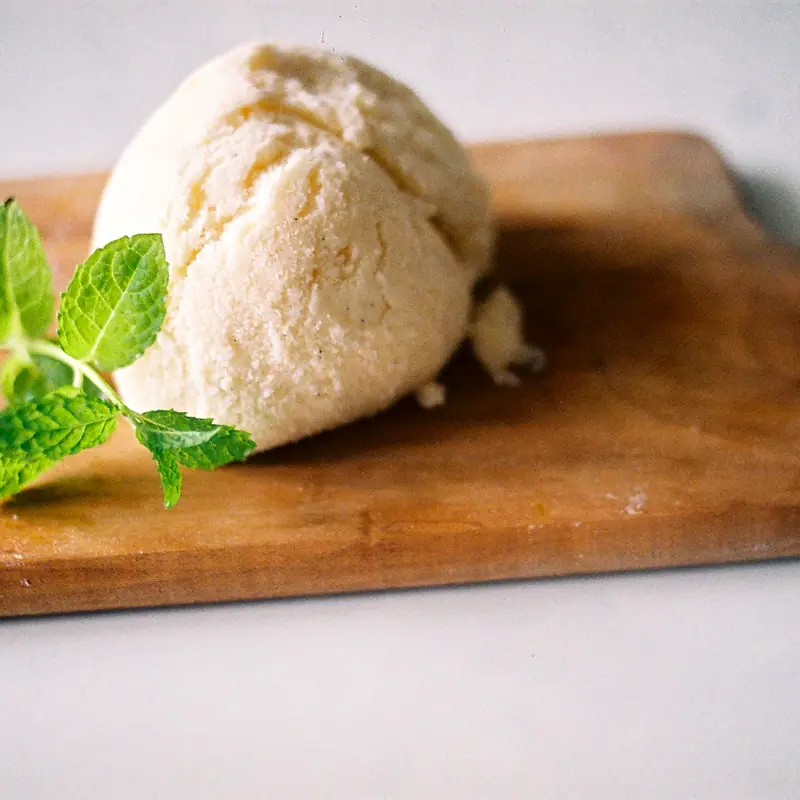 A single pale scoop of vanilla ice cream on a wooden board with a sprig of mint