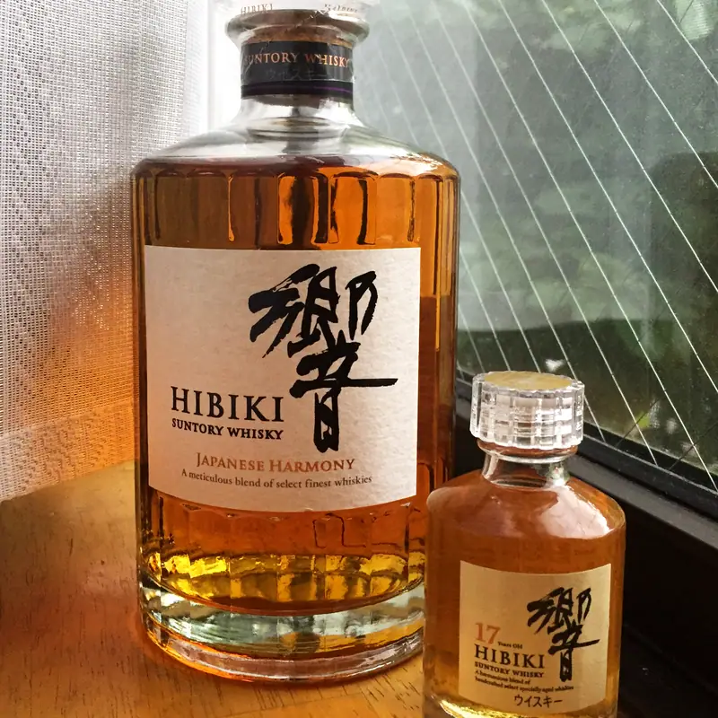 A bottle of Hibiki Japanese blended whisky beside a smaller bottle, backlit by a window