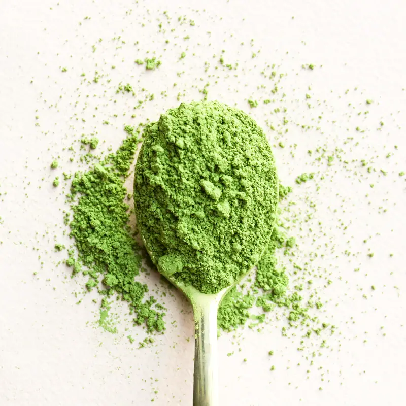 A spoonful of bright green matcha powder spilled onto a pale surface