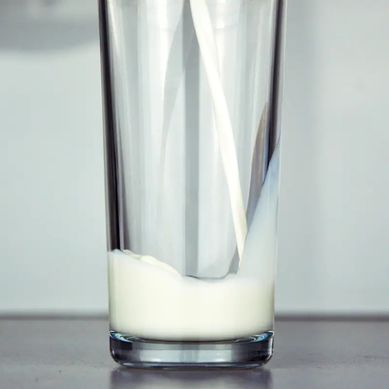 White milk being poured into a tall plain glass, starting to pool at the bottom
