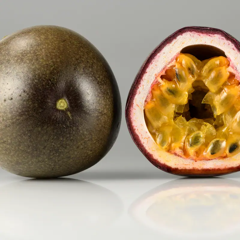 A whole purple passion fruit beside a halved fruit showing its orange pulp and seeds